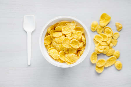 Cornflakes in white bowl with spoon on white wooden background. Top view. Copy, empty space for text.の写真素材