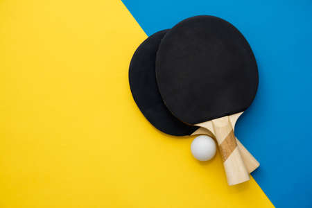 Two table tennis rackets and ball on blue and yellow background. Top view. Copy, empty space for text.の写真素材