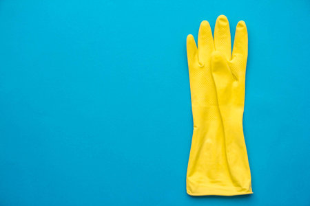 Yellow rubber glove for cleaning hang on blue background. Top view. Minimalist Style. Copy, empty space for text.の写真素材
