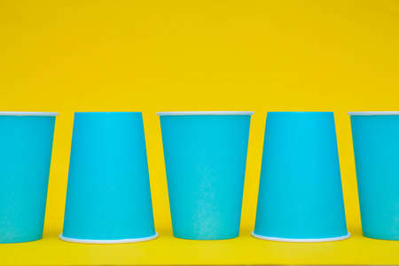 Pattern from blue paper disposable cups on yellow background. Set for party. Top view. Minimalist Style. Copy, empty space for text.の写真素材