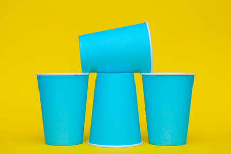 Pyramid of blue paper disposable cups on yellow background. Set for party. Copy, empty space for text.の写真素材