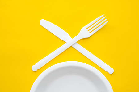 Plastic white spoon and fork on yellow background. Cooking utensil. Cutlery sign. Top view. Minimalist Style. Copy, empty space for text.の写真素材