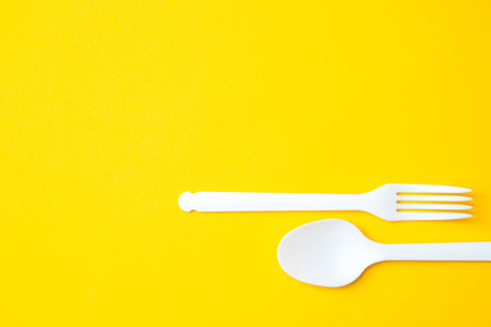 Plastic white spoon and fork on yellow background. Cooking utensil. Cutlery sign. Top view. Minimalist Style. Copy, empty space for text.の写真素材