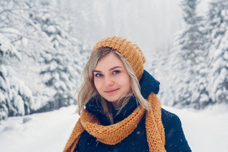 Beautiful young girl in a winter forest. Winter portrait of girl dressed in cap and scarf. Place for text or advertising.の写真素材