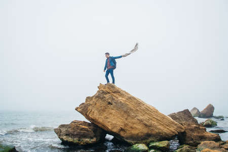 Traveler man with backpack standing on sandy beach in the middle of rocks against sea background. Place for text or advertising.の写真素材