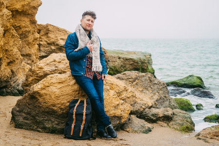 Traveler man with backpack standing on sandy beach in the middle of rocks against sea background. Place for text or advertising.の写真素材