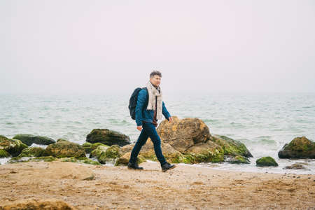Traveler man with backpack standing on sandy beach in the middle of rocks against sea background. Place for text or advertising.の写真素材