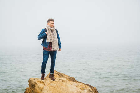 Traveler man with backpack standing on sandy beach in the middle of rocks against sea background. Place for text or advertising.の写真素材
