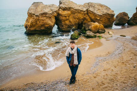 Traveler man with backpack standing on sandy beach in the middle of rocks against sea background. Place for text or advertising.の写真素材