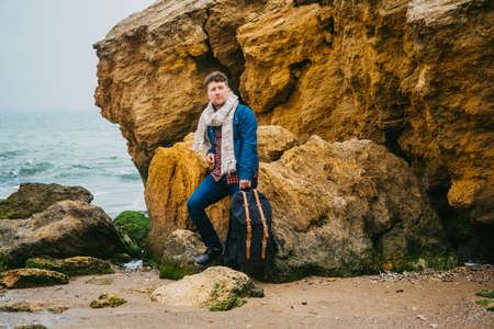 Traveler man with backpack standing on sandy beach in the middle of rocks against sea background. Place for text or advertising.の写真素材