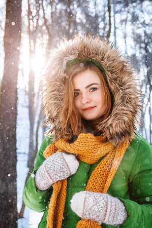 Beautiful young girl in a winter forest. Winter portrait of women dressed in mittens and scarf. Place for text or advertising.の写真素材