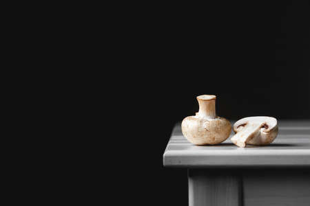 Mushrooms champignons lie in a row on a white table on a dark background. Place for text or advertising.の写真素材