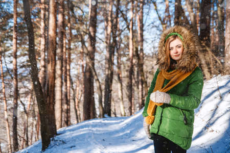 Beautiful young girl in a winter forest. Winter portrait of women dressed in mittens and scarf. Place for text or advertising.の写真素材