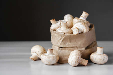 Mushrooms champignons in paper bag on a white wooden table. Place for text or advertising.の写真素材
