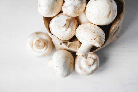 Mushrooms champignons in paper bag on a white wooden table. Place for text or advertising.の写真素材