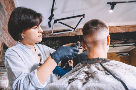 Beautiful woman hairdresser shaves the client's head with a electric trimmer in barber shop. Advertising and barber shop concept.の写真素材