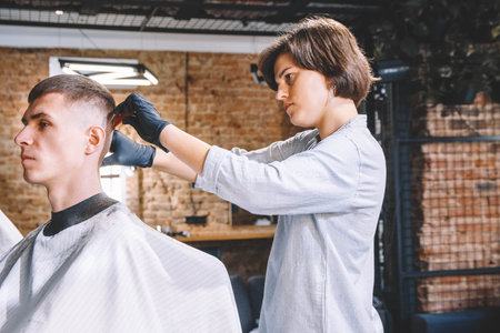 Beautiful woman hairdresser shaves the client's head with a electric trimmer in barber shop. Advertising and barber shop concept.の写真素材
