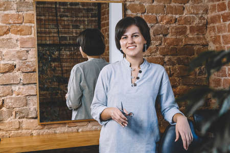 Young beautiful hairdresser woman with scissors in hand in the barbashop salon. Barbershop advertising concept. Place for text or advertising.の写真素材