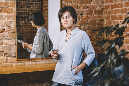 Young beautiful hairdresser woman with scissors in hand in the barbashop salon. Barbershop advertising concept. Place for text or advertising.の写真素材
