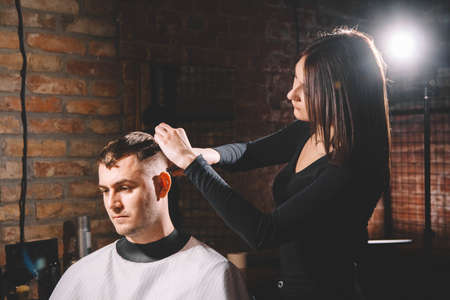 Beautiful female hairdresser cutting client's hair with scissors in a barber shop. Concept of advertising and hairdressing.の写真素材
