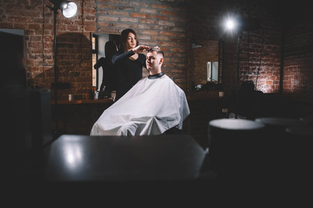 Beautiful female hairdresser cutting client's hair with scissors in a barber shop. Concept of advertising and hairdressing.の写真素材