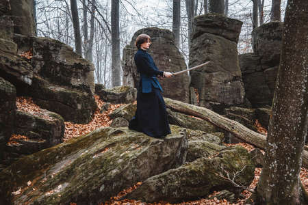 Man practicing kendo with bamboo sword on waterfall, rocks and forest background. Place for text or advertising.の写真素材