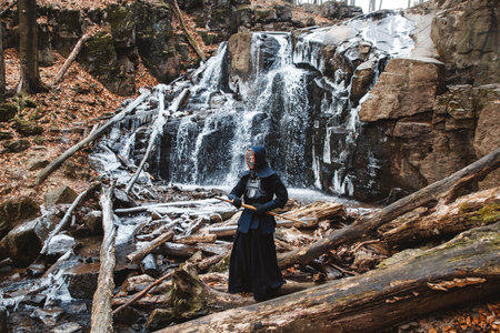 Man practicing kendo with bamboo sword on waterfall, rocks and forest background. Place for text or...