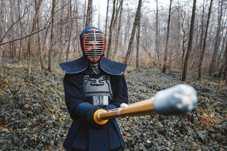 Man practicing kendo with bamboo sword on waterfall, rocks and forest background. Place for text or...
