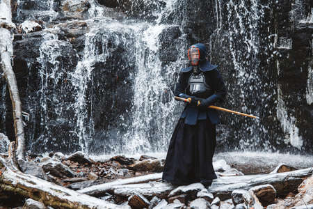 Man practicing kendo with bamboo sword on waterfall, rocks and forest background. Place for text or advertising.の写真素材