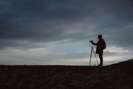 Traveler man with camera on tripod standing on the background of the mountain and a lake makes a photo landscape. Travel lifestyle concept. Copy, empty space for text.の写真素材