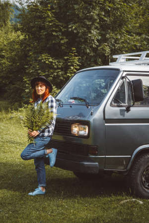 Beautiful woman in hat holding fern leaves on car background. Traveler holiday concept, travel adventure. Copy, empty space for text.の写真素材