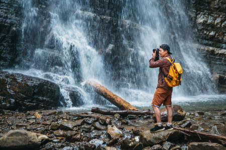 Traveler man with a yellow backpack standing on the background of a waterfall. Travel lifestyle conceptの写真素材