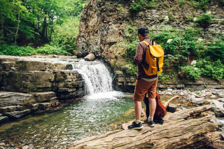 Traveler man with a yellow backpack standing on the background of a waterfall. Travel lifestyle conceptの写真素材