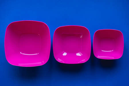 Set of pink plates on blue background. Plastic utensils for the kitchen. Copy, empty space for text.の写真素材