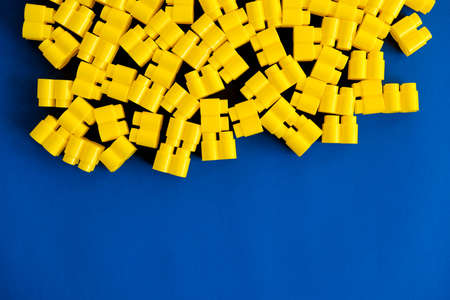 Yellow plastic building blocks on blue and yellow background. Pieces and elements of constructor. Parts of bright small spare parts for toys. Top view. Copy, empty space for text.の写真素材