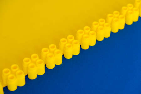 Yellow plastic building blocks on blue and yellow background. Pieces and elements of constructor. Parts of bright small spare parts for toys. Top view. Copy, empty space for text.の写真素材