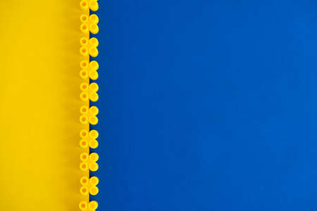 Yellow plastic building blocks in the shape of a pyramid on yellow background. Background of plastic details building blocks. Parts of bright small spare parts for toys. Copy, empty space for text.の写真素材