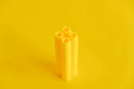 Yellow plastic building blocks in the shape of a pyramid on yellow background. Background of plastic details building blocks. Parts of bright small spare parts for toys. Copy, empty space for text.の写真素材