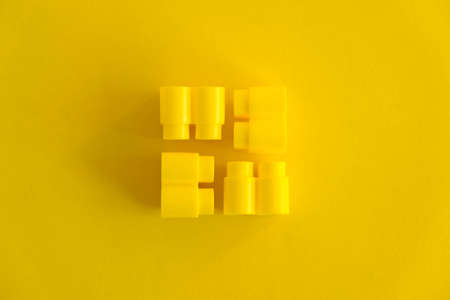 Yellow plastic building blocks in the shape of a pyramid on yellow background. Background of plastic details building blocks. Parts of bright small spare parts for toys. Copy, empty space for text.の写真素材