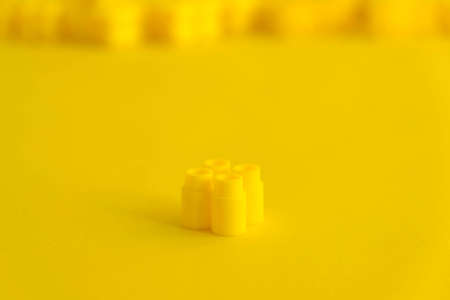 Yellow plastic building blocks in the shape of a tower on yellow background. Background of plastic details building blocks. Parts of bright small spare parts for toys. Copy, empty space for text.の写真素材