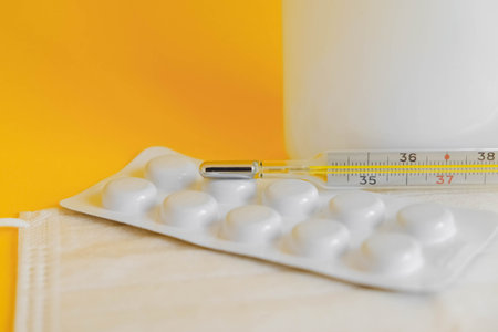 Medical disposable mask, pills and a mercury thermometer on a yellow background. Copy, empty space...