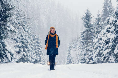 Beautiful young woman in a winter forest. Winter portrait of woman dressed in cap and scarf. Place for text or advertising.の写真素材