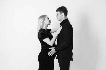 Pregnant woman and her husband hugging and holding onto your stomach in black clothes on a white background. Black and white picture. Beautiful married couple. Copy, empty space for text.の写真素材