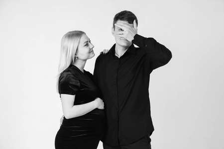 Pregnant woman and her husband hugging and holding onto your stomach in black clothes on a white background. Black and white picture. Beautiful married couple. Copy, empty space for text.の写真素材
