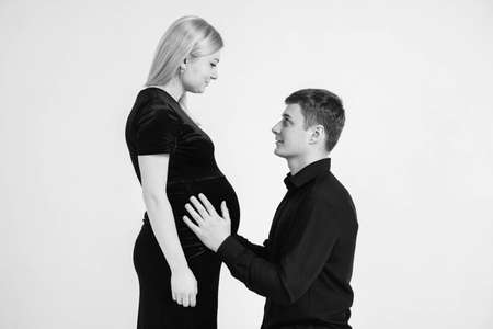 Pregnant woman and her husband holding hands in black clothes on a white background. Black and white picture. Beautiful married couple. Copy, empty space for text.の写真素材