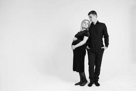 Pregnant woman and her husband holding hands in black clothes on a white background. Black and white picture. Beautiful married couple. Copy, empty space for text.の写真素材