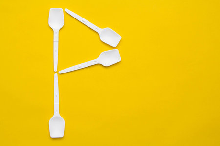 White plastic spoons in the form of letter P on yellow background. Top view. Copy, empty space for...
