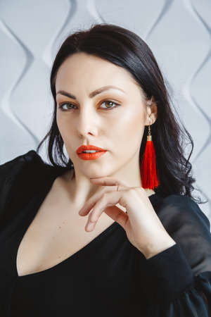 Beautiful woman in black dress posing near chair in bright studio. Place for text or advertising.の写真素材