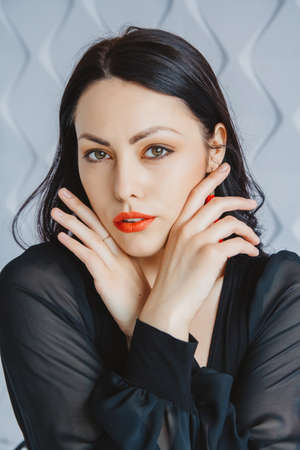Beautiful woman in black dress posing near chair in bright studio. Place for text or advertising.の写真素材