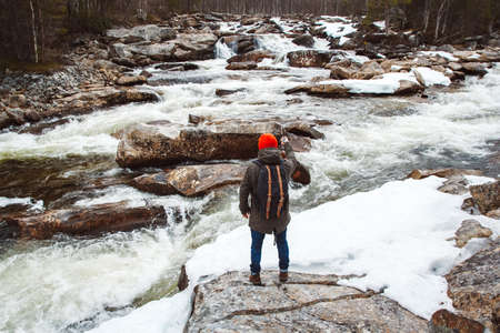Young man with a yellow backpack wearing a red hat standing on a rock on the background of mountain and lake. Space for your text message or promotional content. Travel lifestyle concept.の写真素材